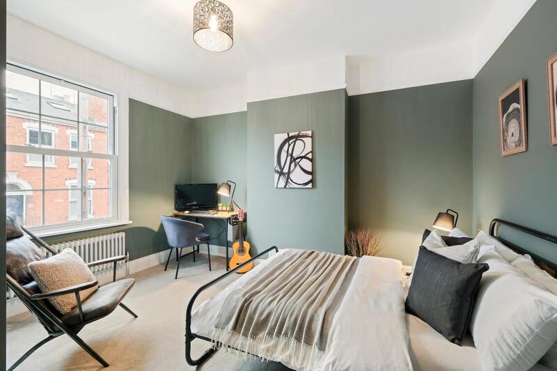 Contemporary bedroom with sage green feature wall, metal bed frame, and desk area