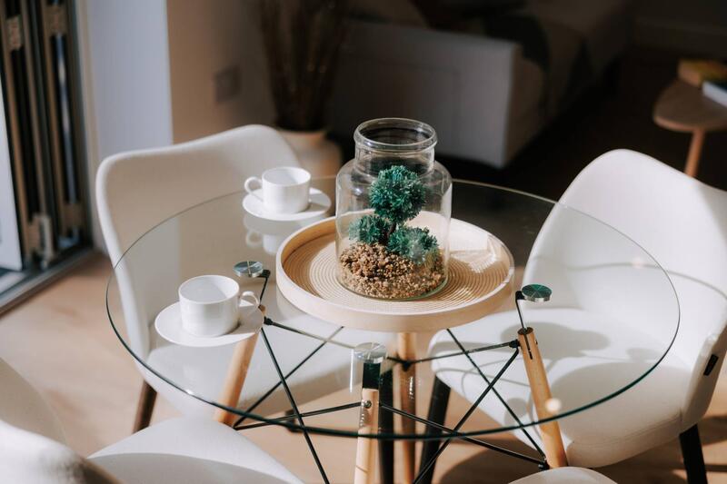Close-up of styled glass dining table with terrarium centrepiece and coffee cups