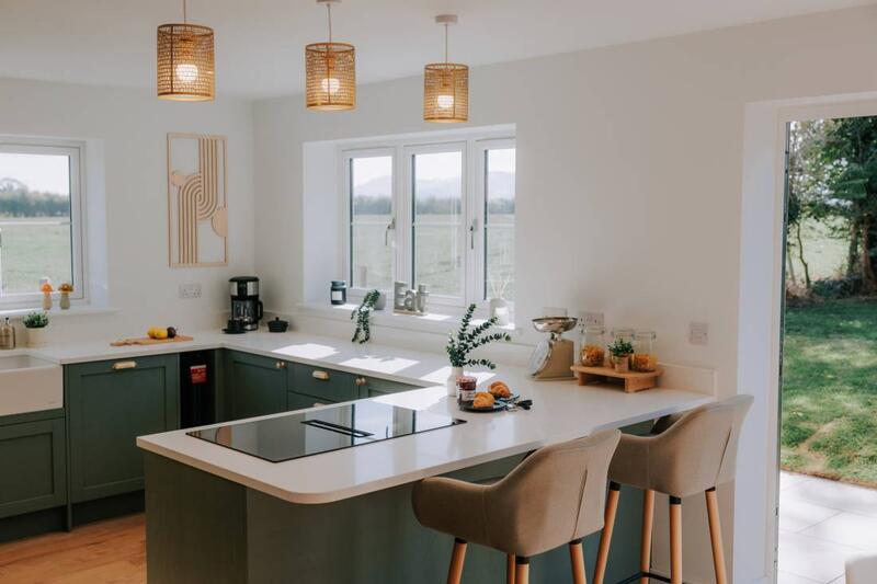 Green shaker kitchen with breakfast bar, rattan pendant lights, and garden views
